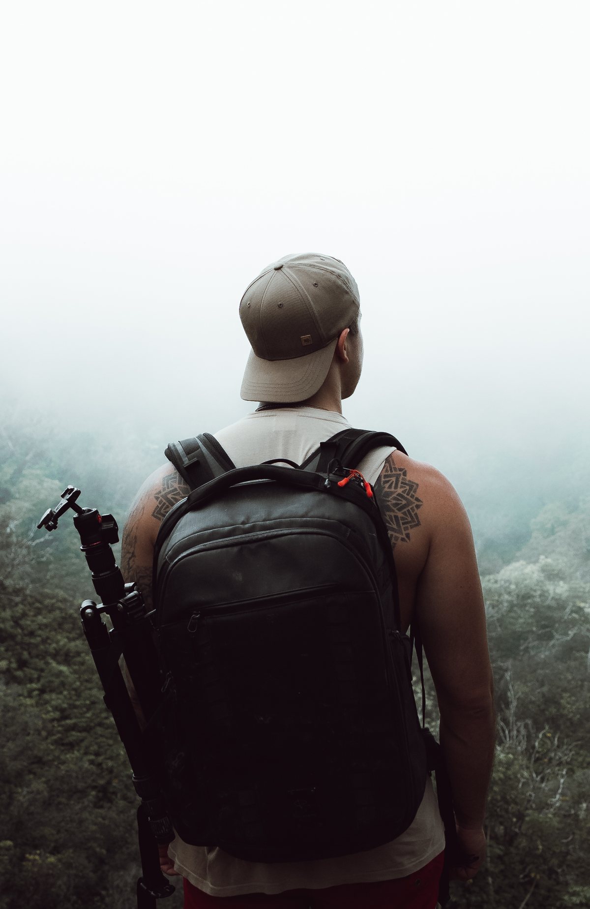 Dre Anderson with a camera pack and tripod, looking out over a misty forest